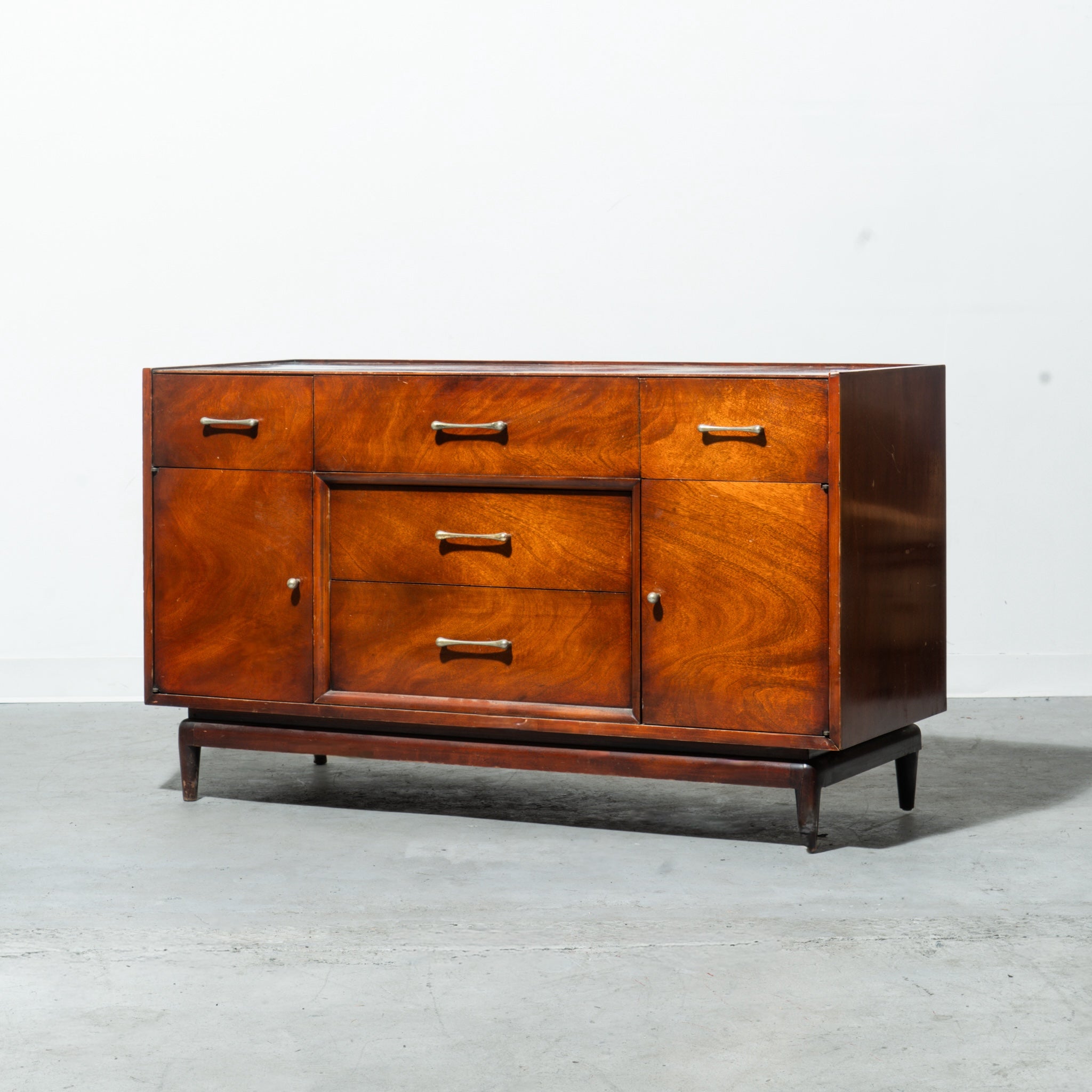 Wooden mid-century modern sideboard credenza with drawers and doors on a gray floor and white wall background
