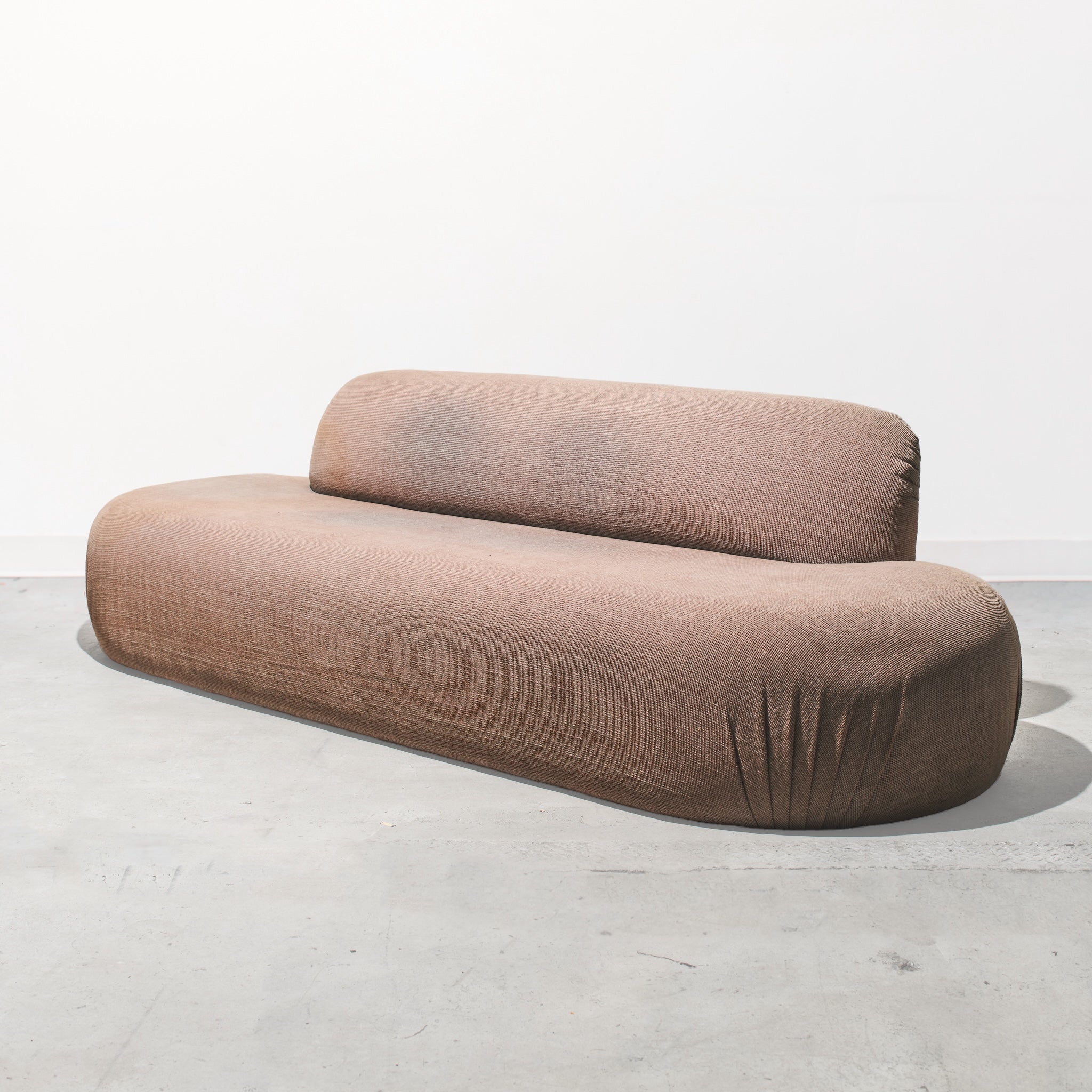 Brown curved sofa on a light gray floor with a white background