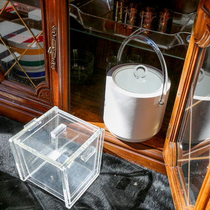 Clear plastic box and white ice cream container on a dark surface with a wooden cabinet in the background.