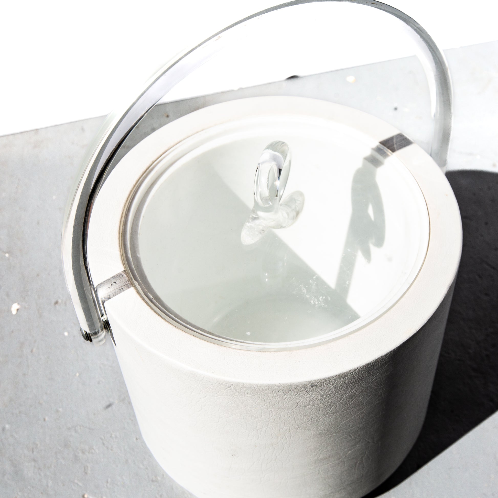 White ceramic jar with a clear glass lid on a light gray surface