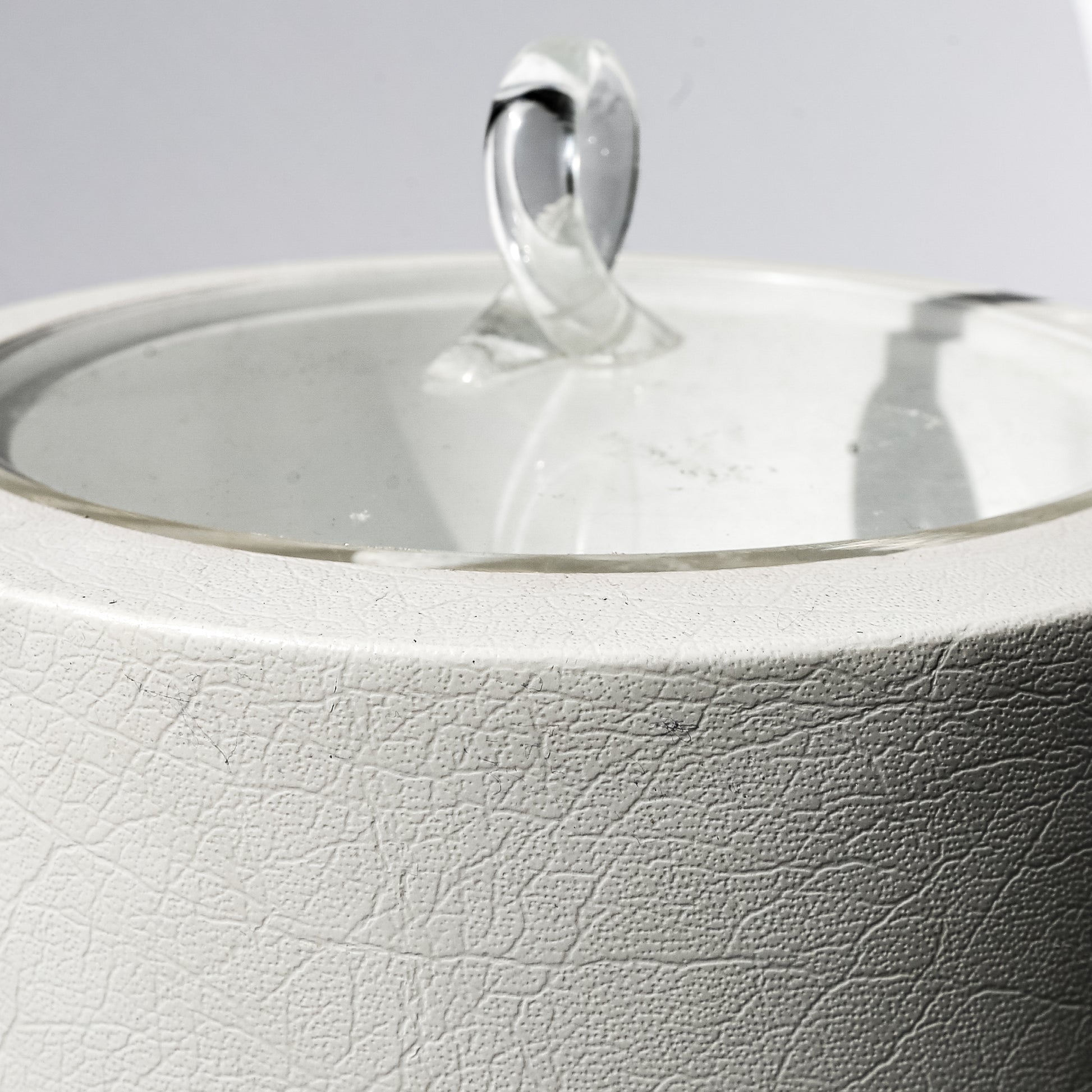 Close-up of a white ceramic teapot with a silver lid and handle on a light gray background.