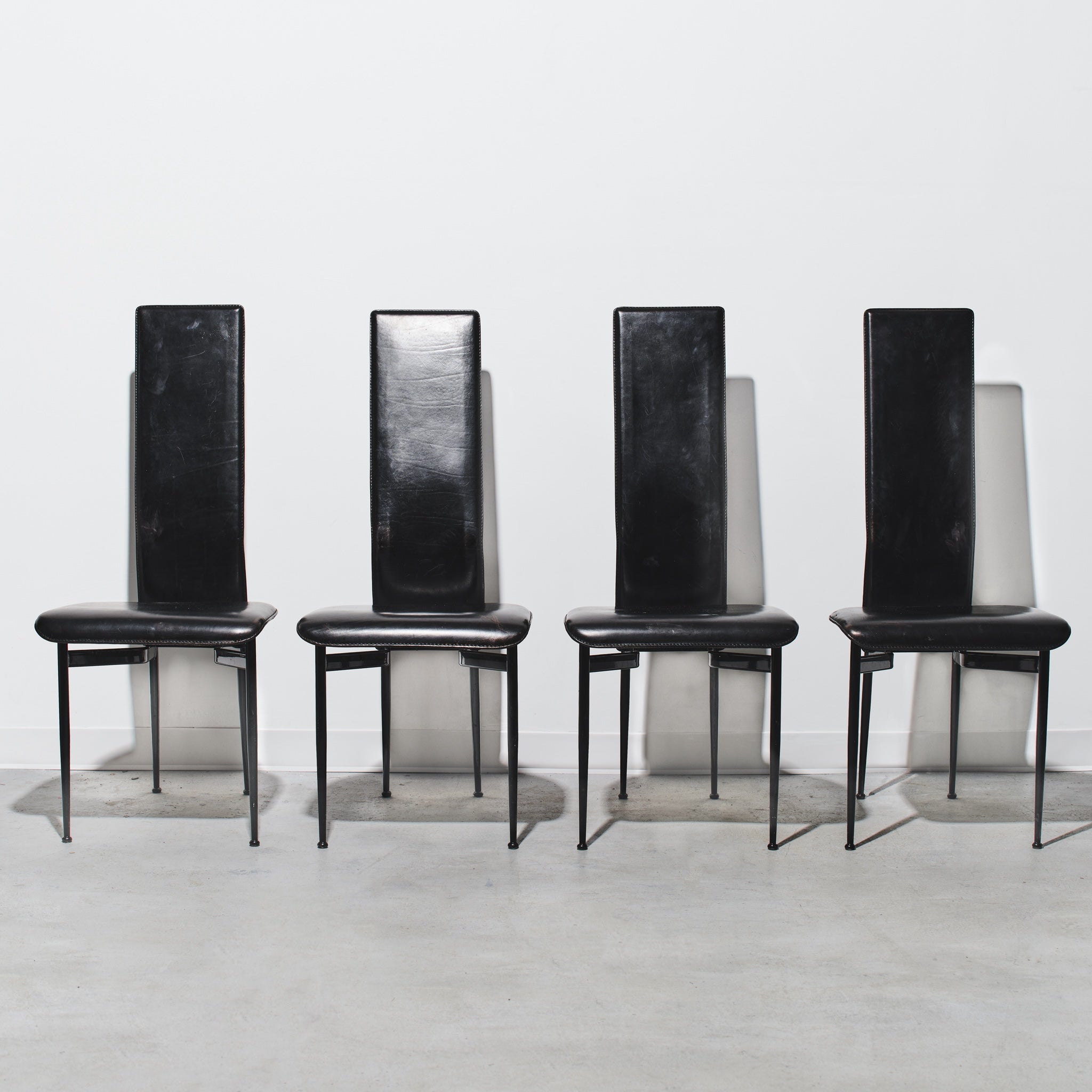 Four black chairs with high backs on a white background
