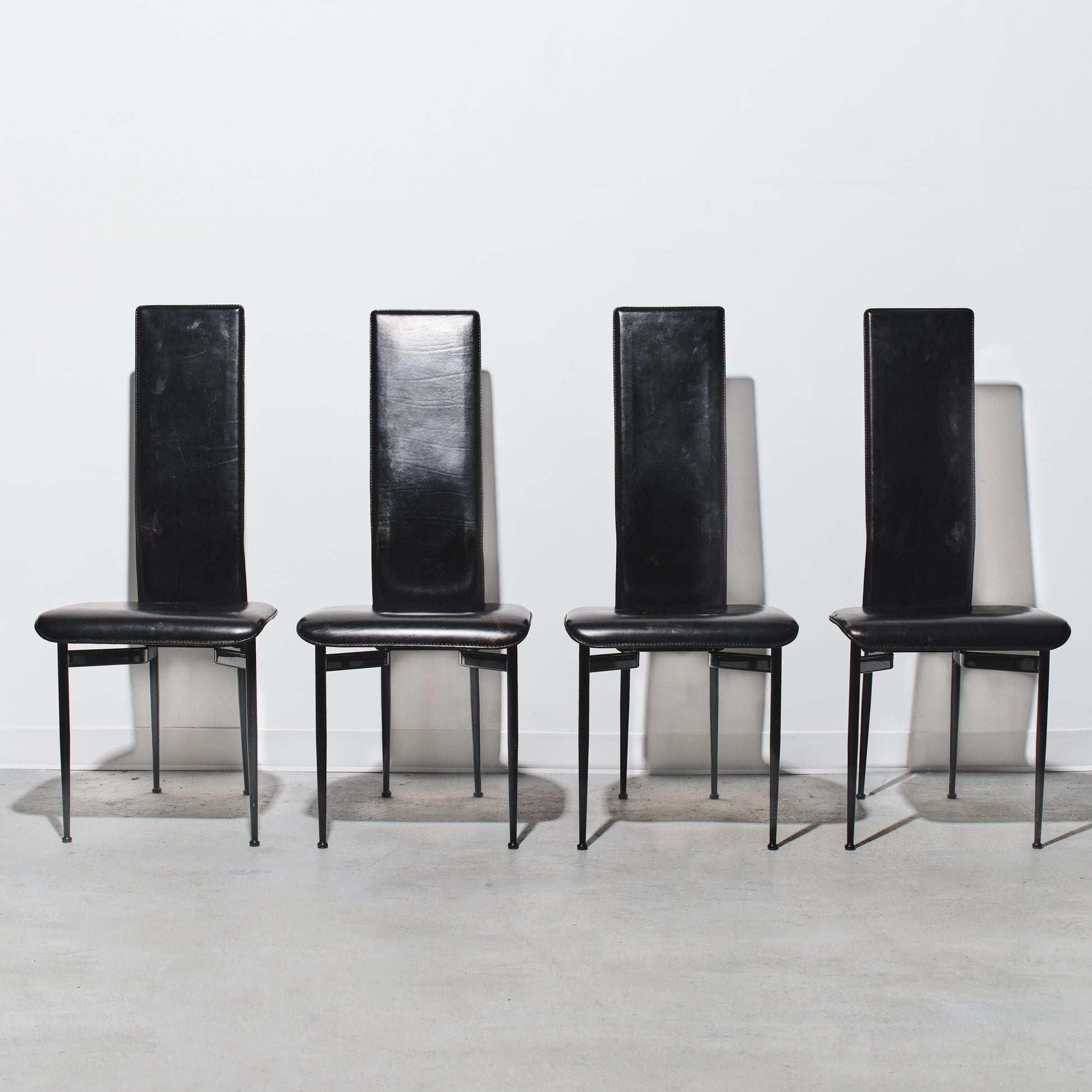 Four black chairs with high backs on a white background