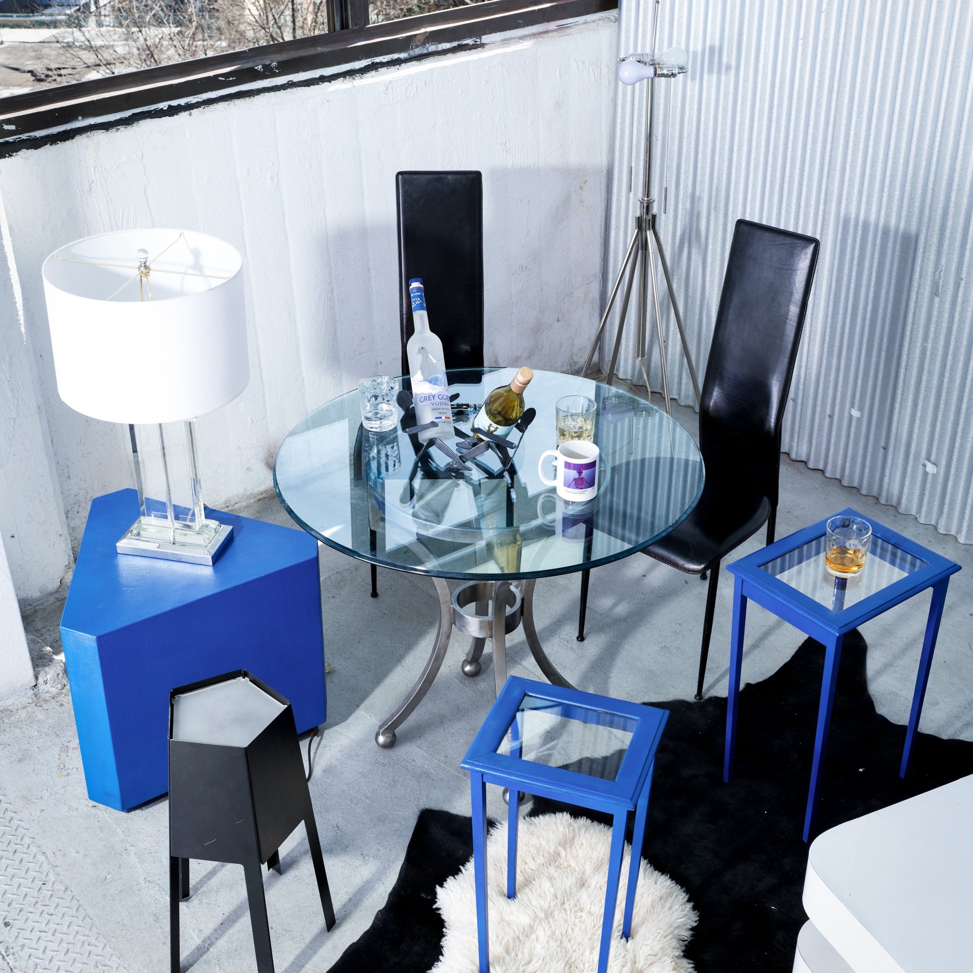 Modern living room with glass table, black chairs, and blue side tables.