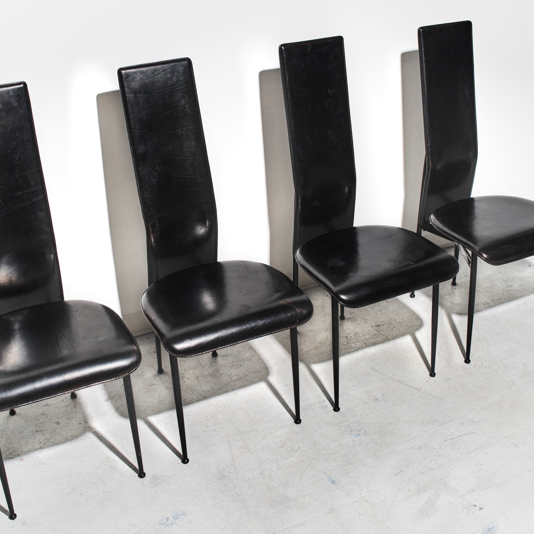 Set of five black chairs with high backs on a concrete floor.