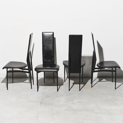Four black chairs with thin legs on a light gray floor and white wall background