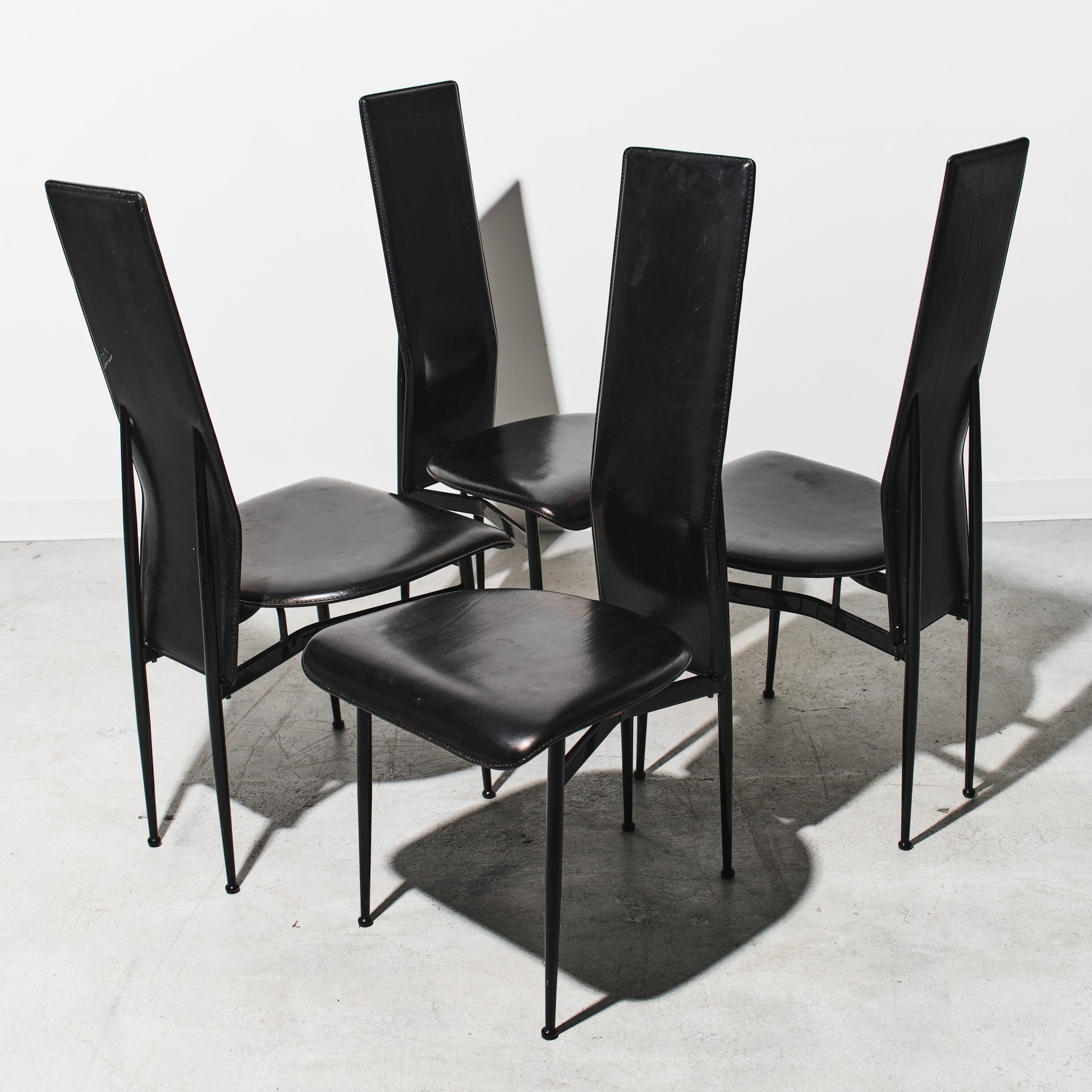 Four black chairs with metal legs on a white floor and wall.
