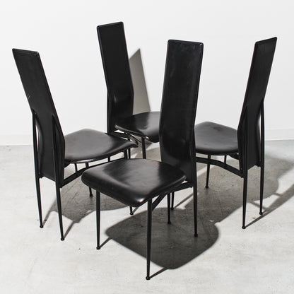 Four black chairs with metal legs on a white floor and wall.