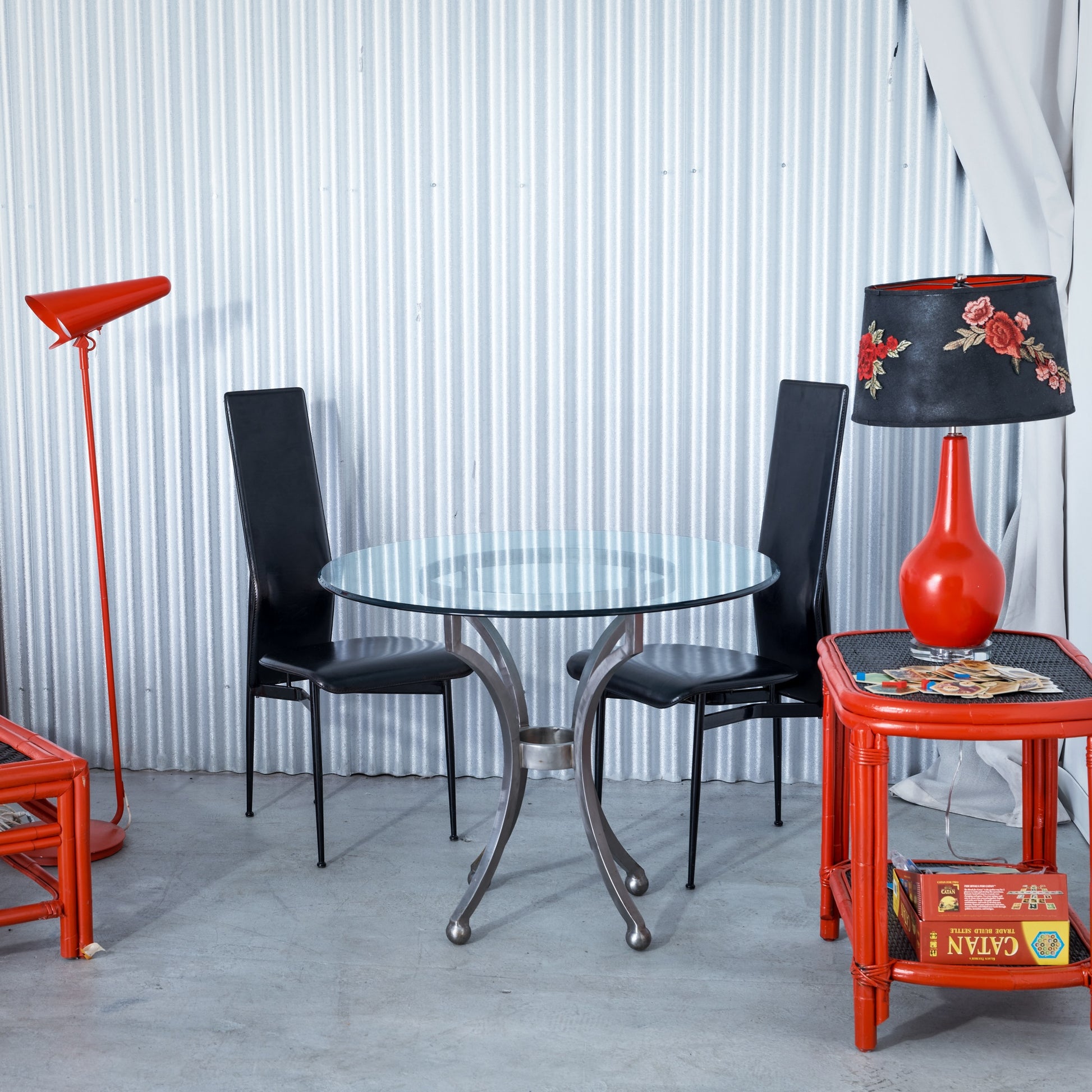 Modern interior with a glass dining table, black chairs, and red lamp against a white paneled wall.