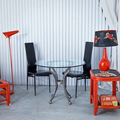 Modern interior with a glass dining table, black chairs, and red lamp against a white paneled wall.