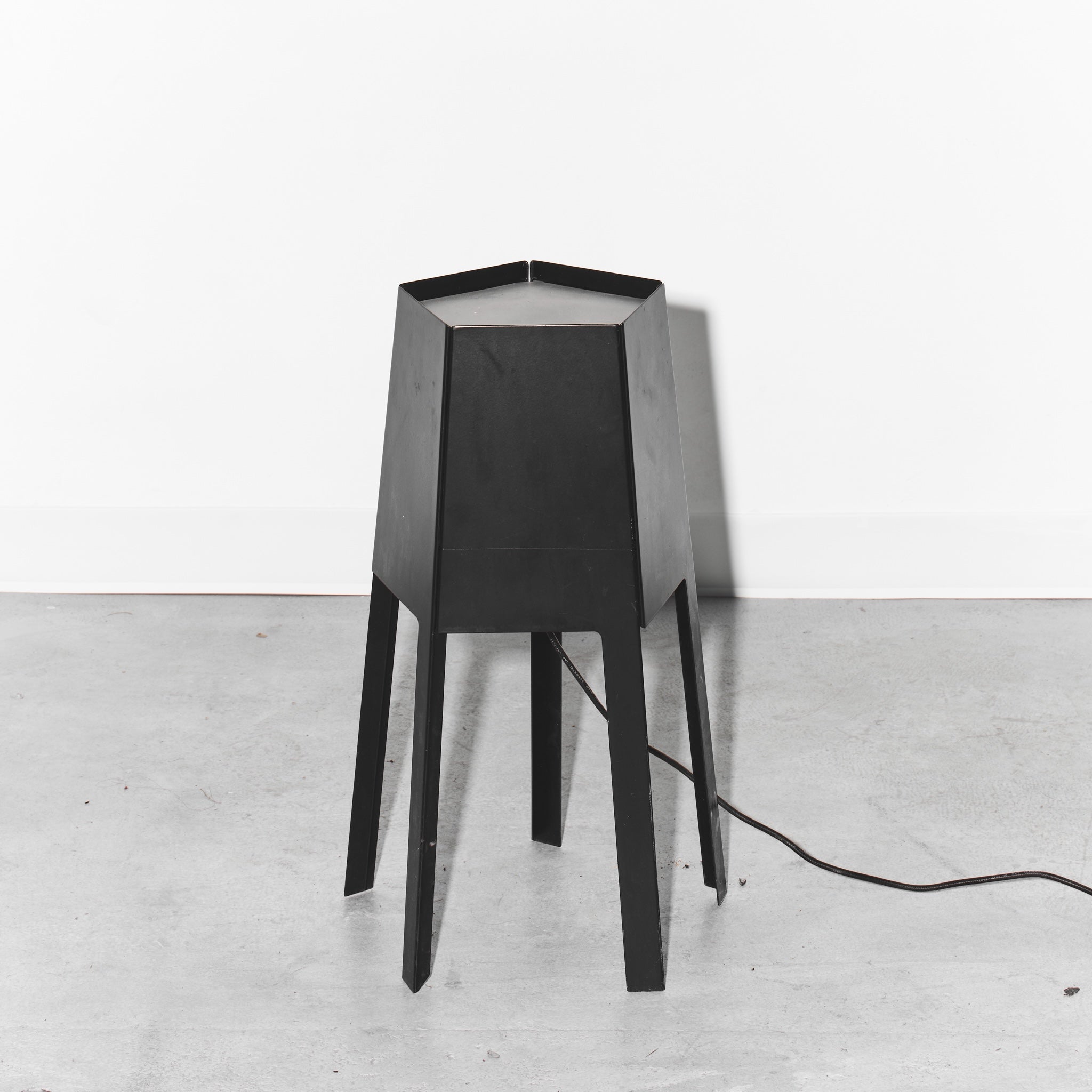 Black geometric table lamp on a white floor with a white wall background