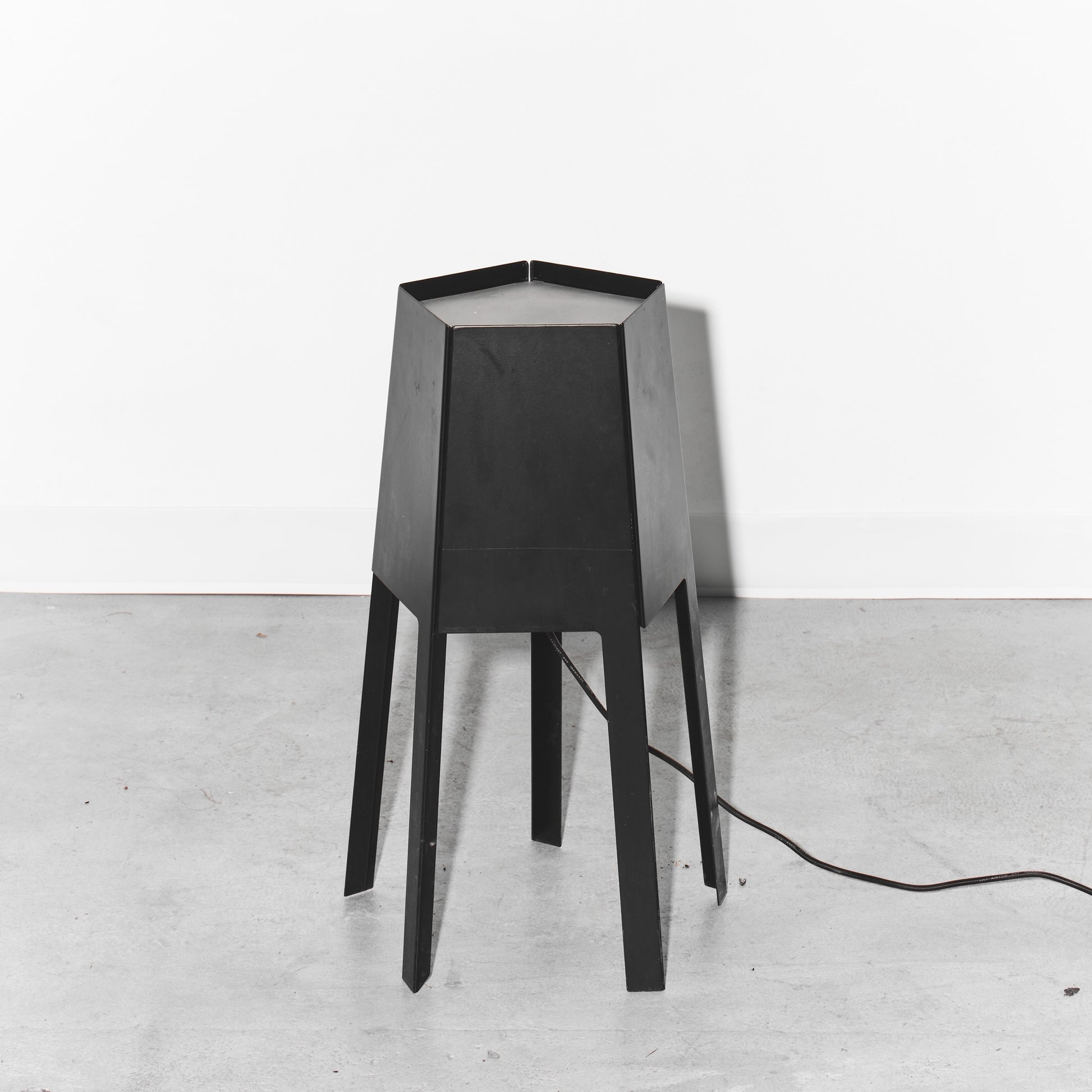 Black geometric table lamp on a white floor with a white wall background