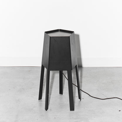 Black geometric table lamp on a white floor with a white wall background