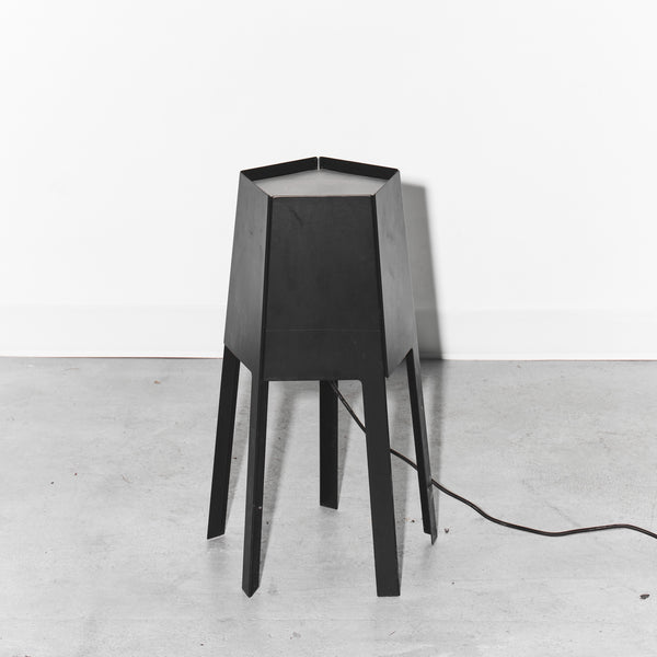 Black geometric table lamp on a white floor with a white wall background