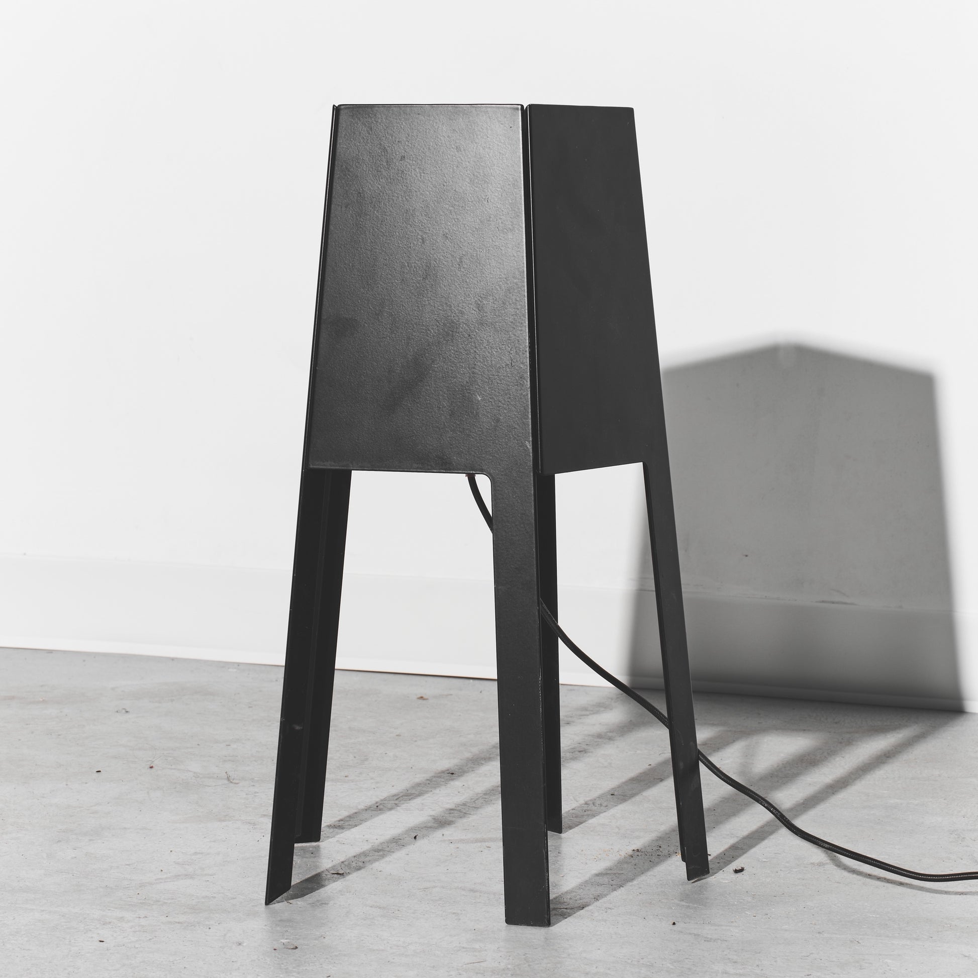 Black lamp with a textured shade on a white floor and light gray wall