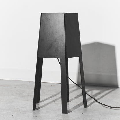 Black lamp with a textured shade on a white floor and light gray wall
