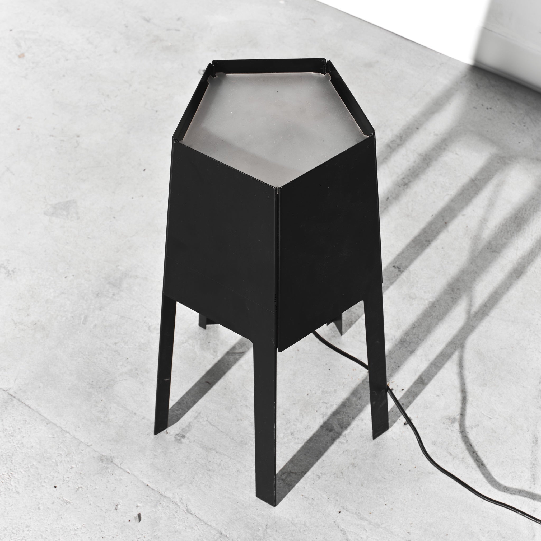 Black hexagonal lamp on a light gray concrete floor