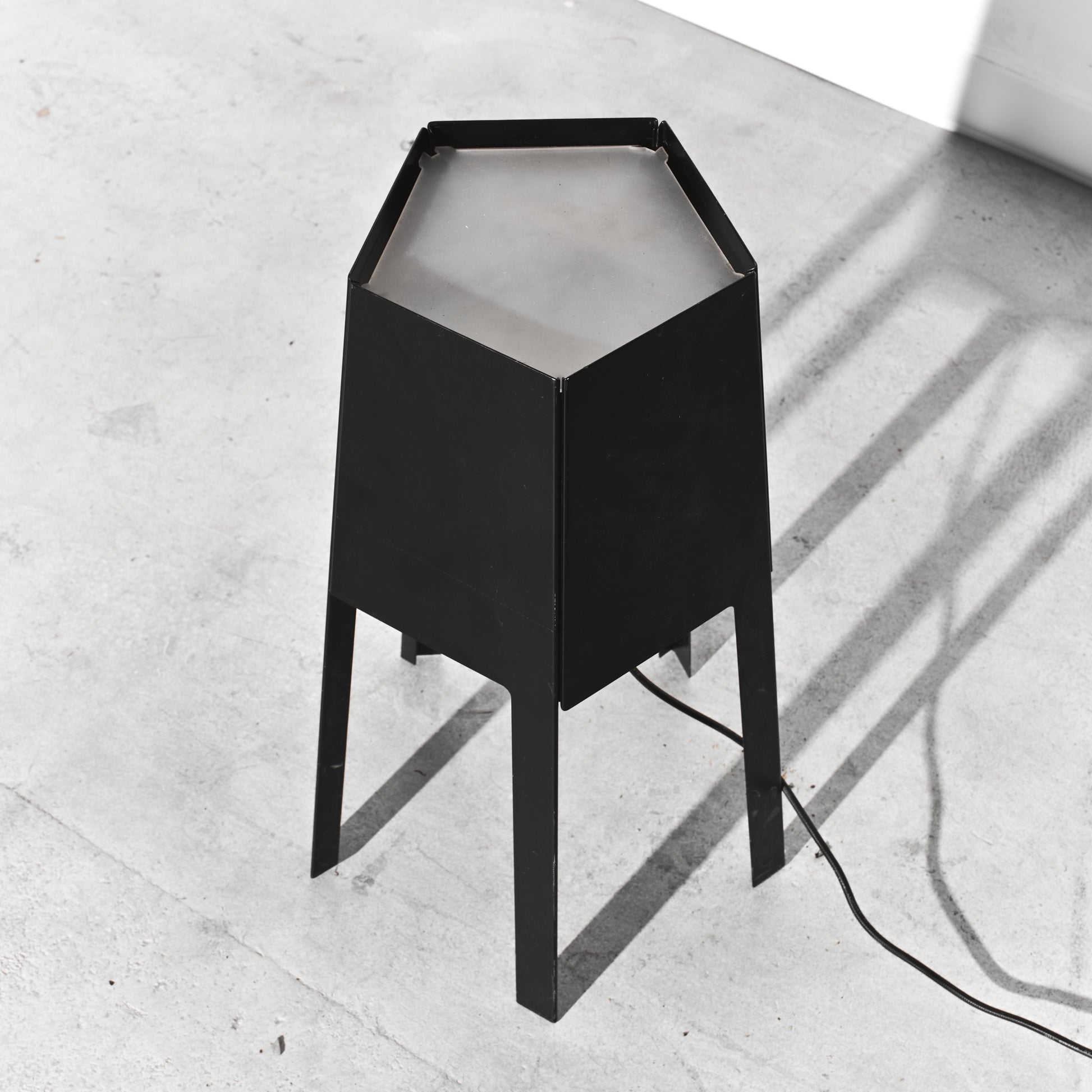 Black hexagonal lamp on a light gray concrete floor