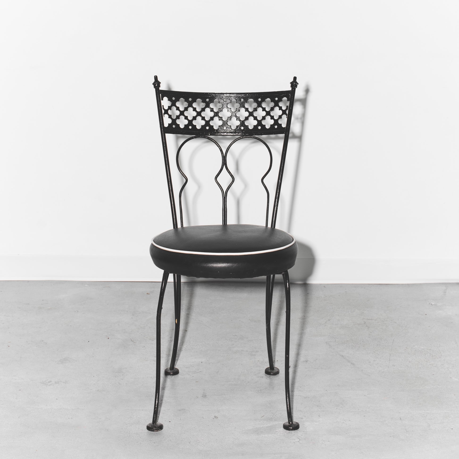 Black metal chair with decorative backrest on a light gray floor and white background
