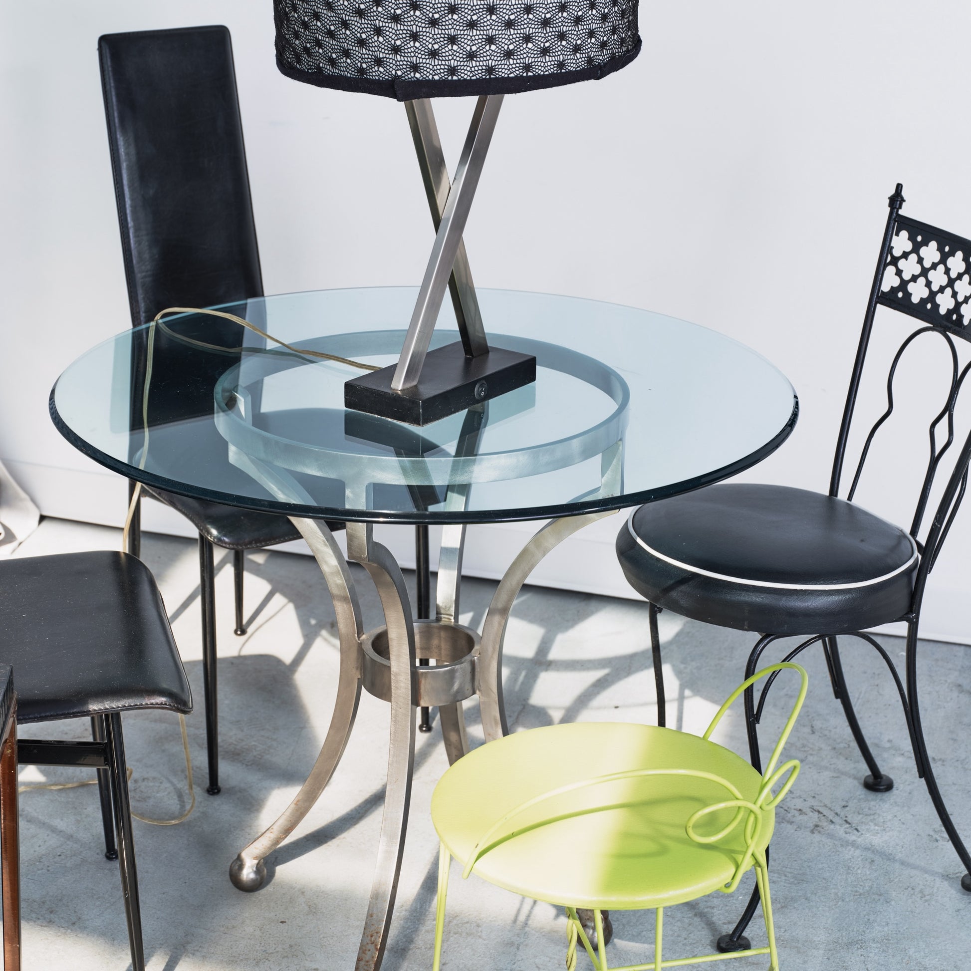 Glass dining table with black chairs and a green chair on a light gray floor.