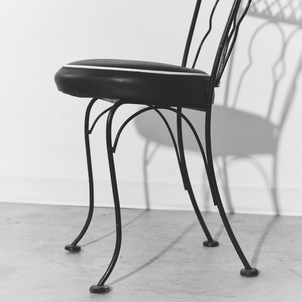 Black metal chair with cushioned seat on a light wooden floor.