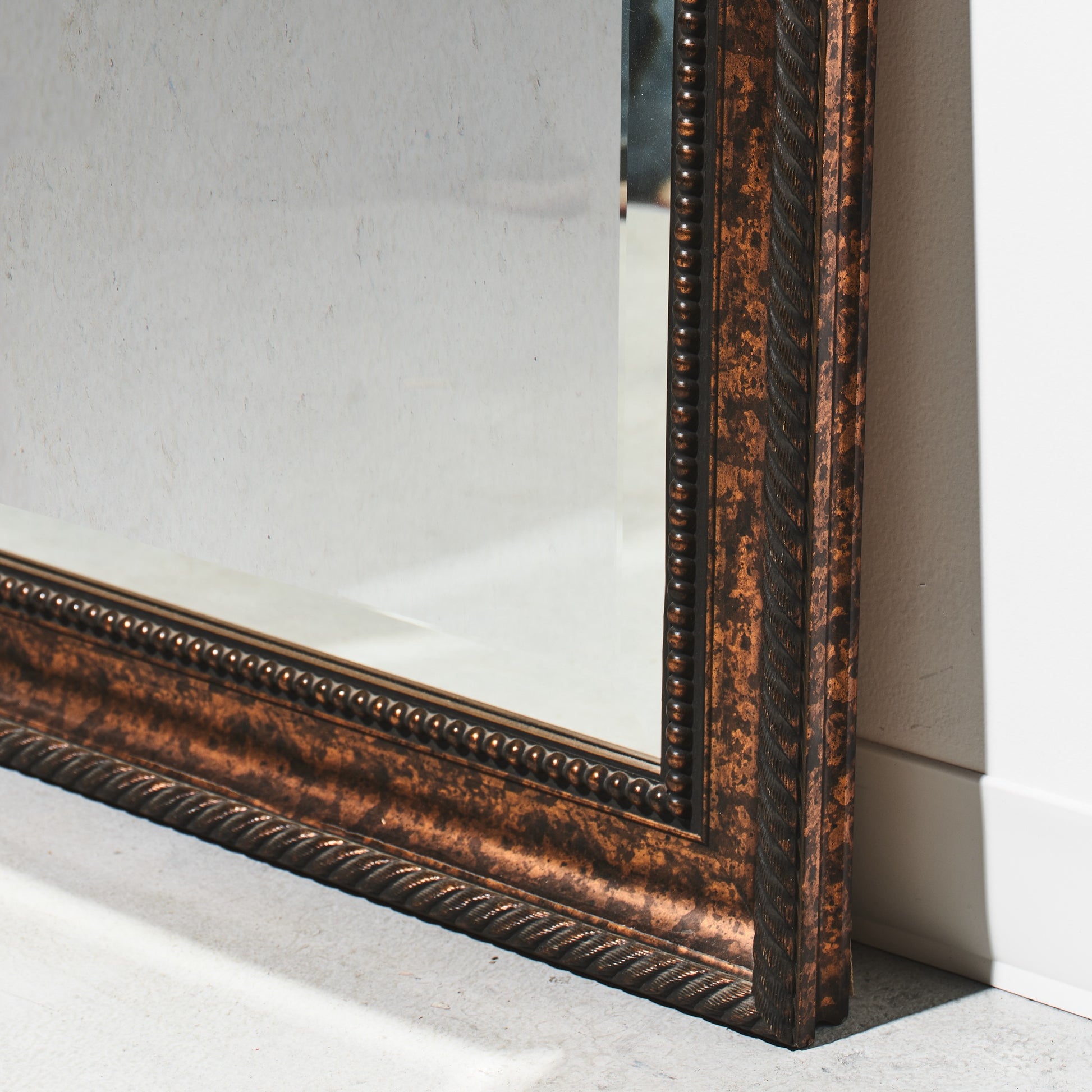 Decorative mirror with a bronze frame on a light gray floor.