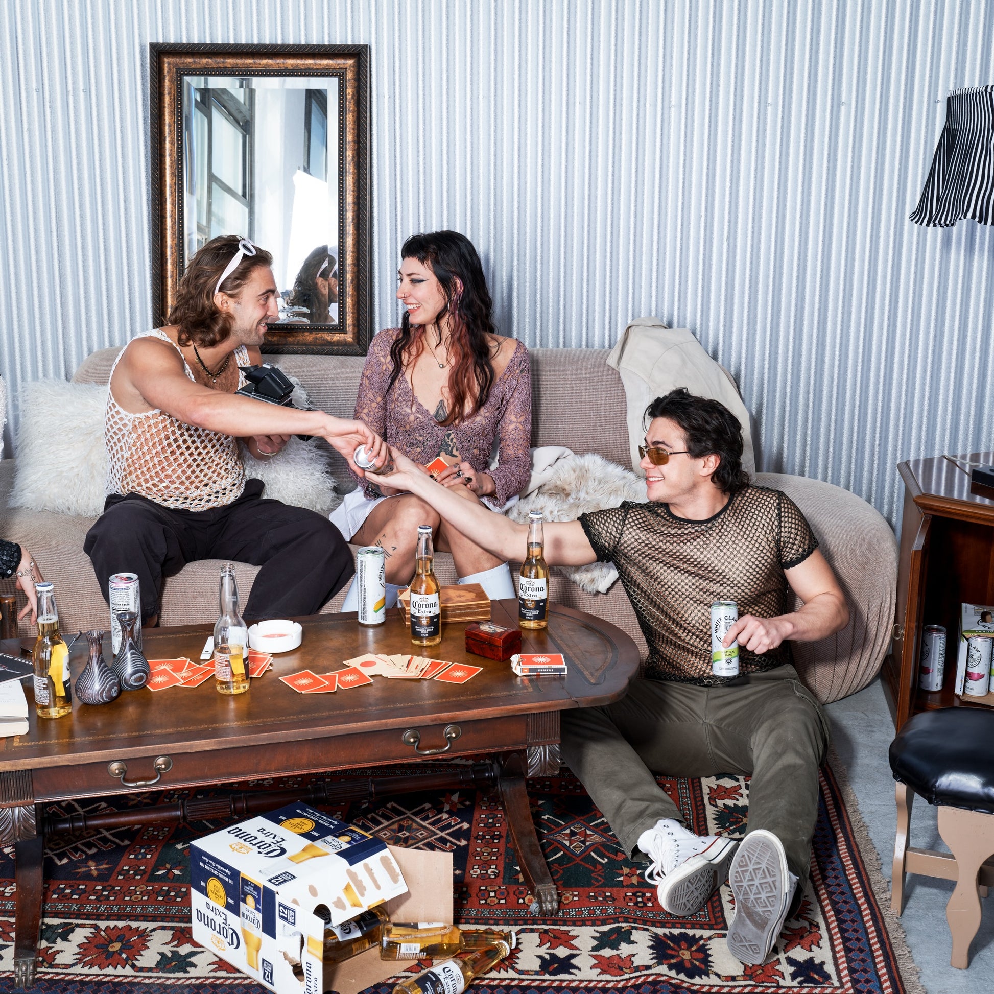 Three people sitting on a couch in a living room with drinks and cards.