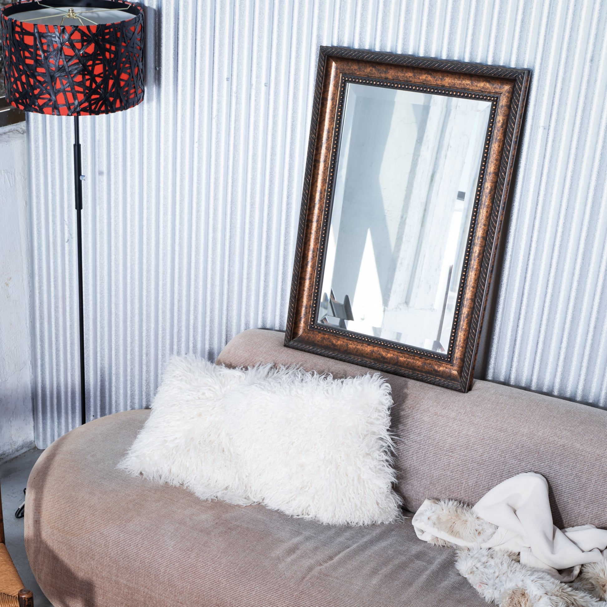Living room with a gray sofa, white pillow, and decorative mirror on a corrugated metal wall.