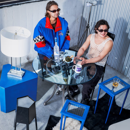 Two people sitting at a glass table with drinks and snacks in a modern room.