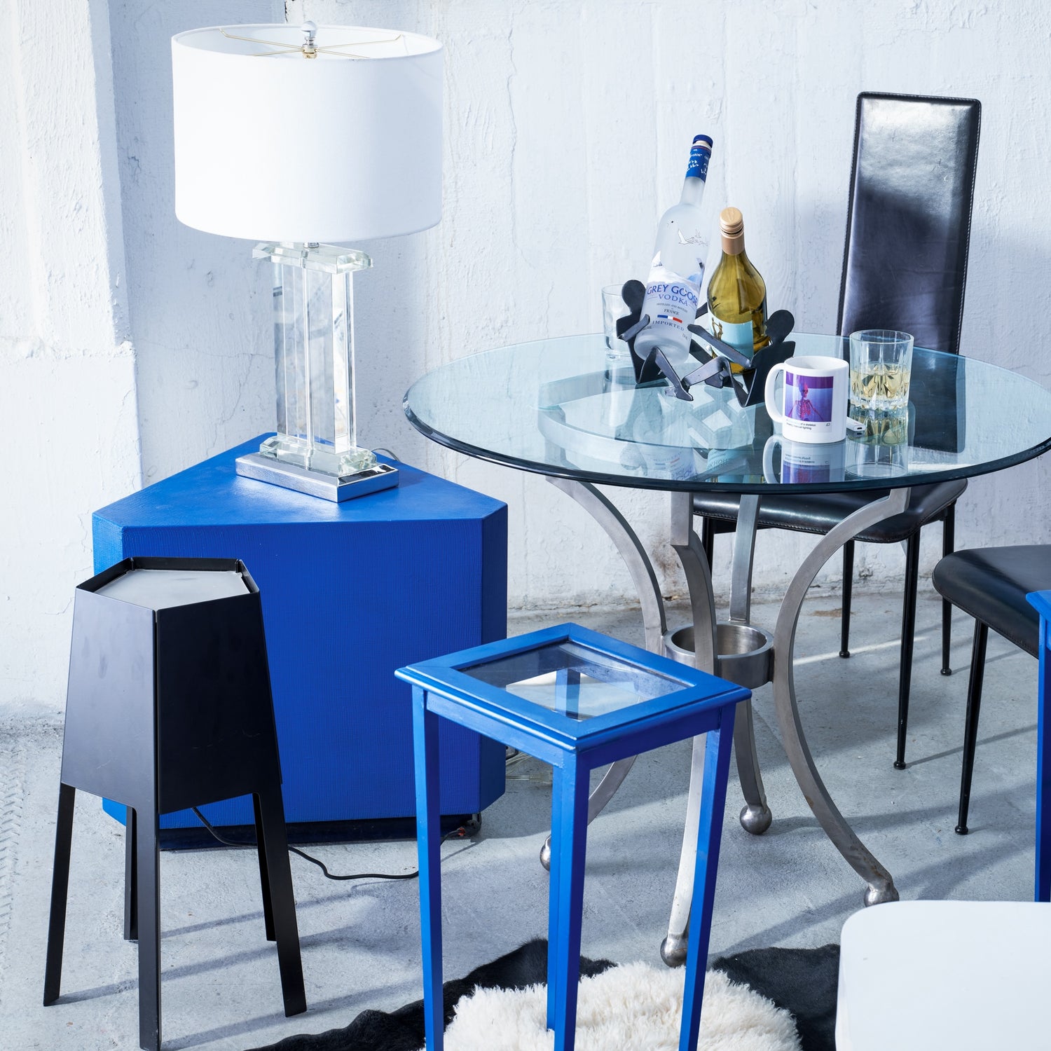 Modern dining room with a glass table, black chairs, and blue side tables.