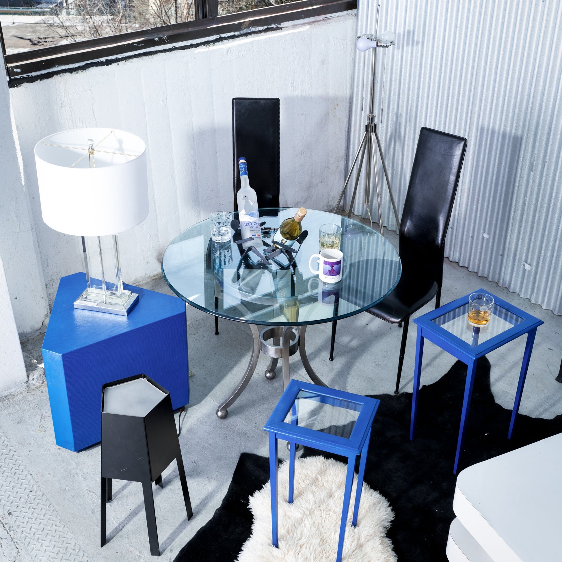 Modern dining area with glass table, black chairs, and blue side tables.