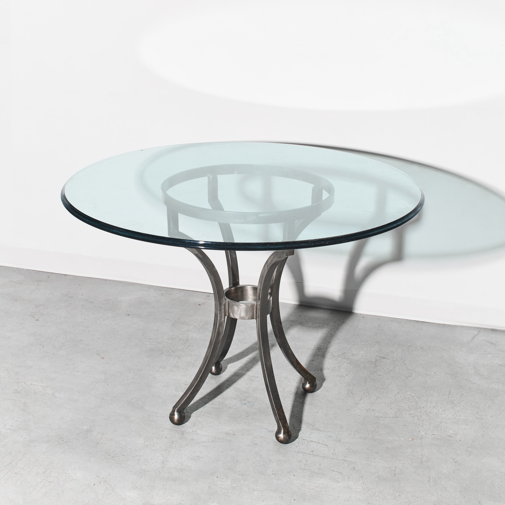 Round glass table with metal base on a light gray floor and white wall background