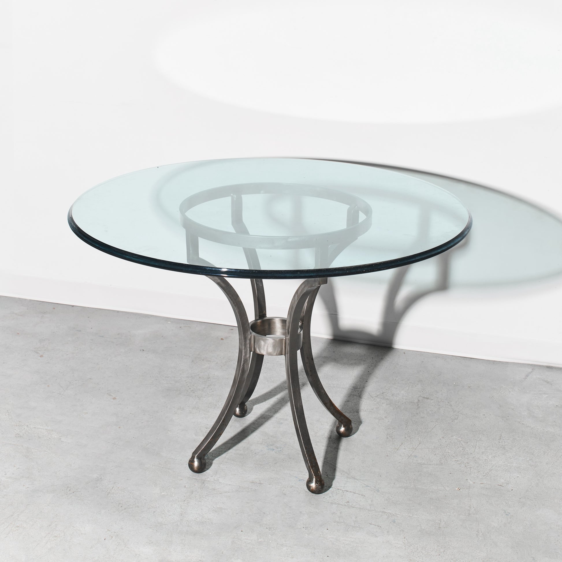 Round glass table with metal base on a light gray floor and white wall background