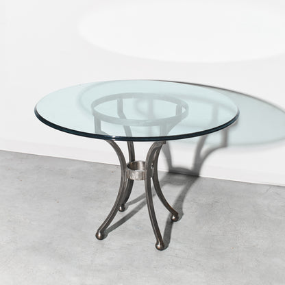 Round glass table with metal base on a light gray floor and white wall background