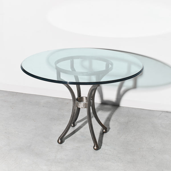 Round glass table with metal base on a light gray floor and white wall background