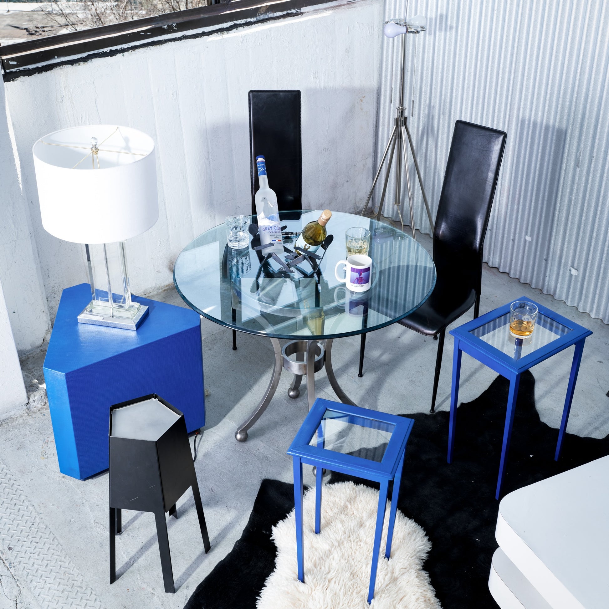 Modern dining area with glass table, black chairs, and blue side tables.
