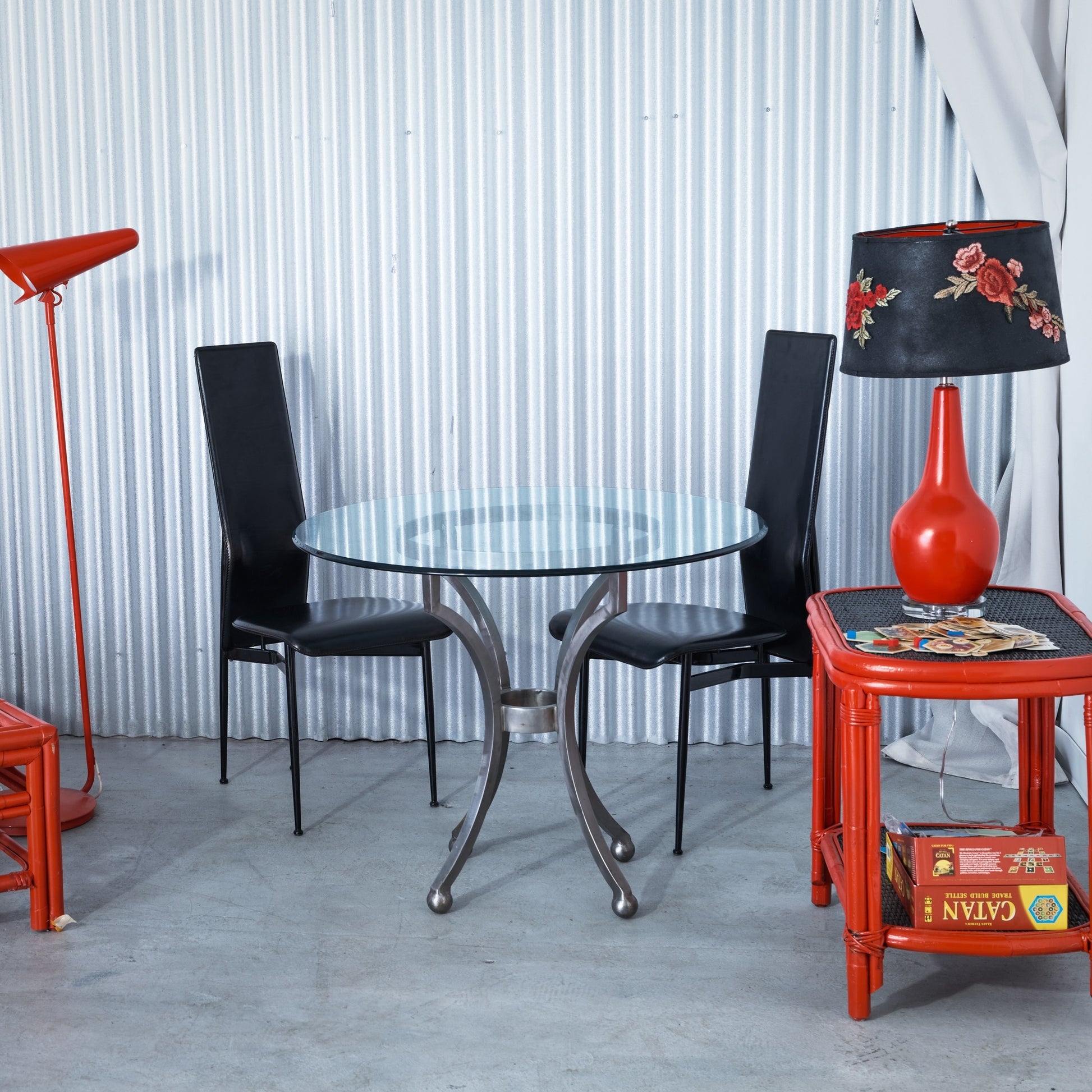 Dining area with a glass table, black chairs, and a red side table with a lamp.