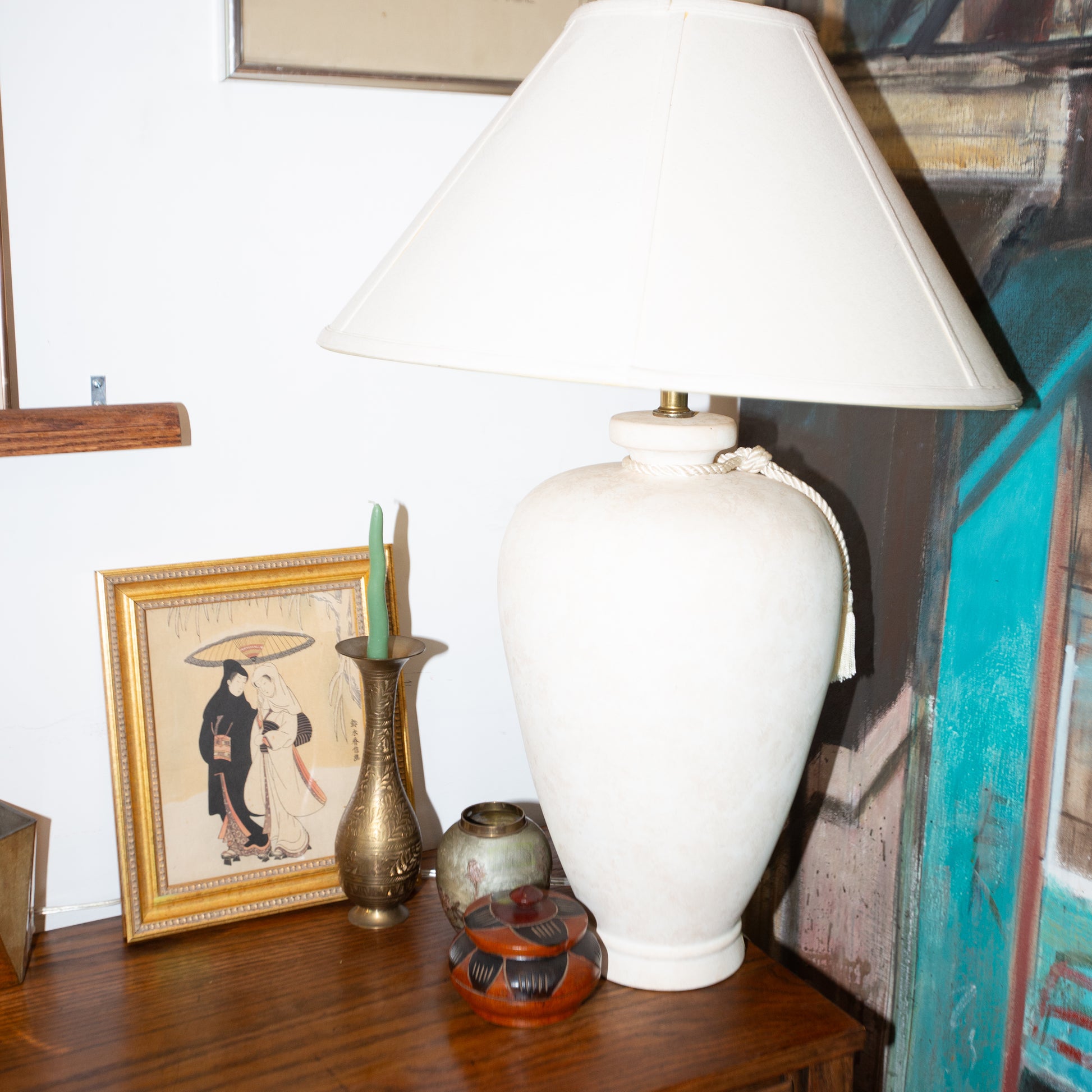 White lamp on a wooden surface with decorative items and a framed picture in the background.