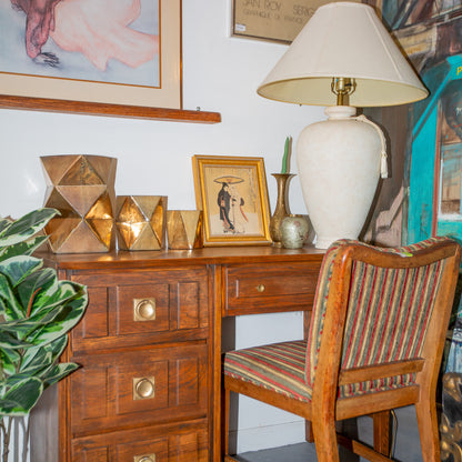 Wooden desk with lamp, framed picture, and chair in a room with artwork on the wall.