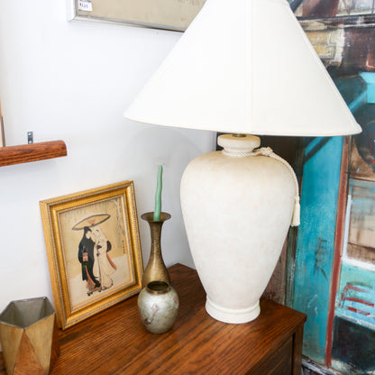 White lamp on a wooden surface with decorative items and a colorful painting in the background.
