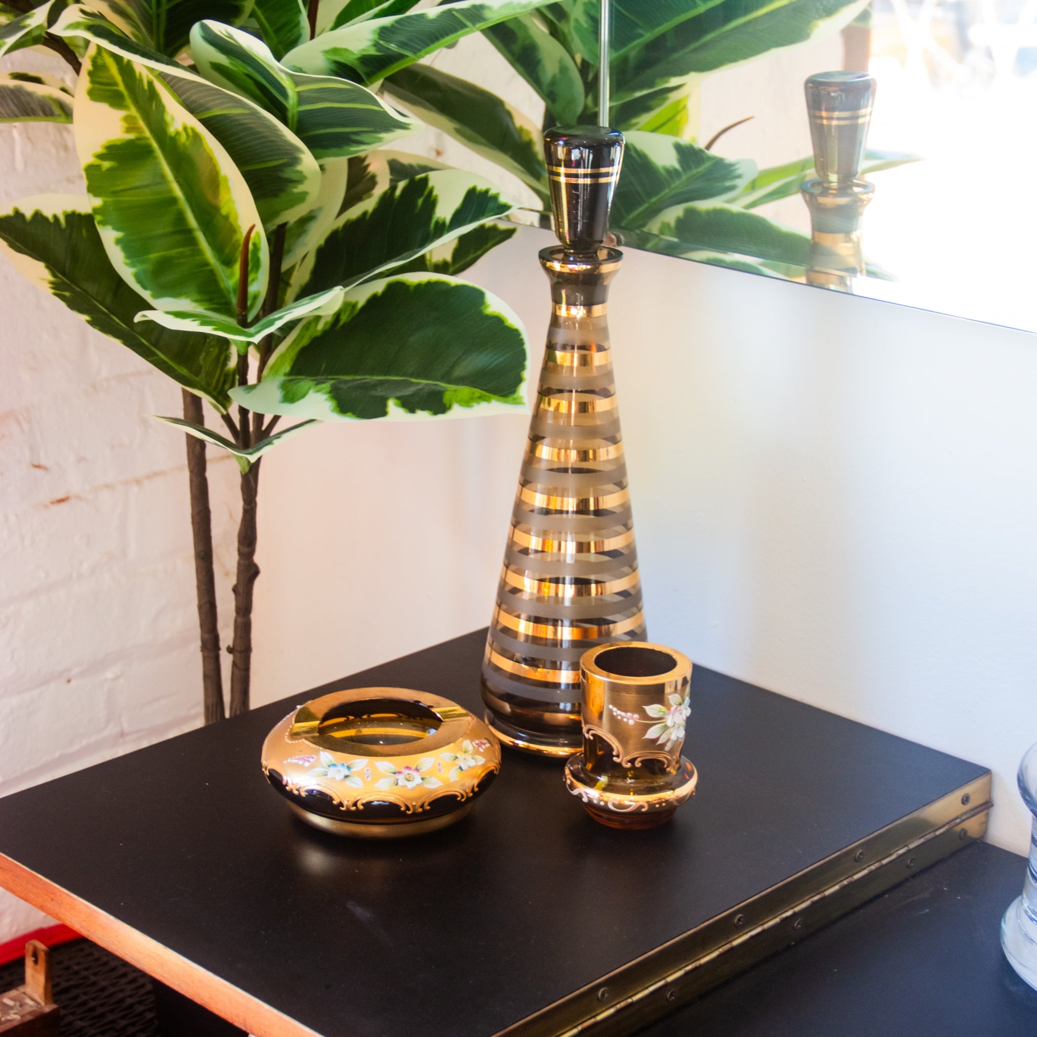 Decorative vases and ashtray on a black surface with a plant in the background