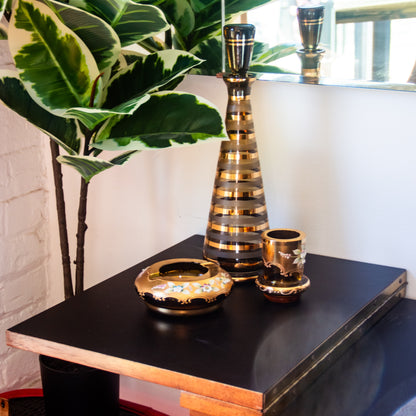 Decorative vases and bowl on a black surface with a plant in the background