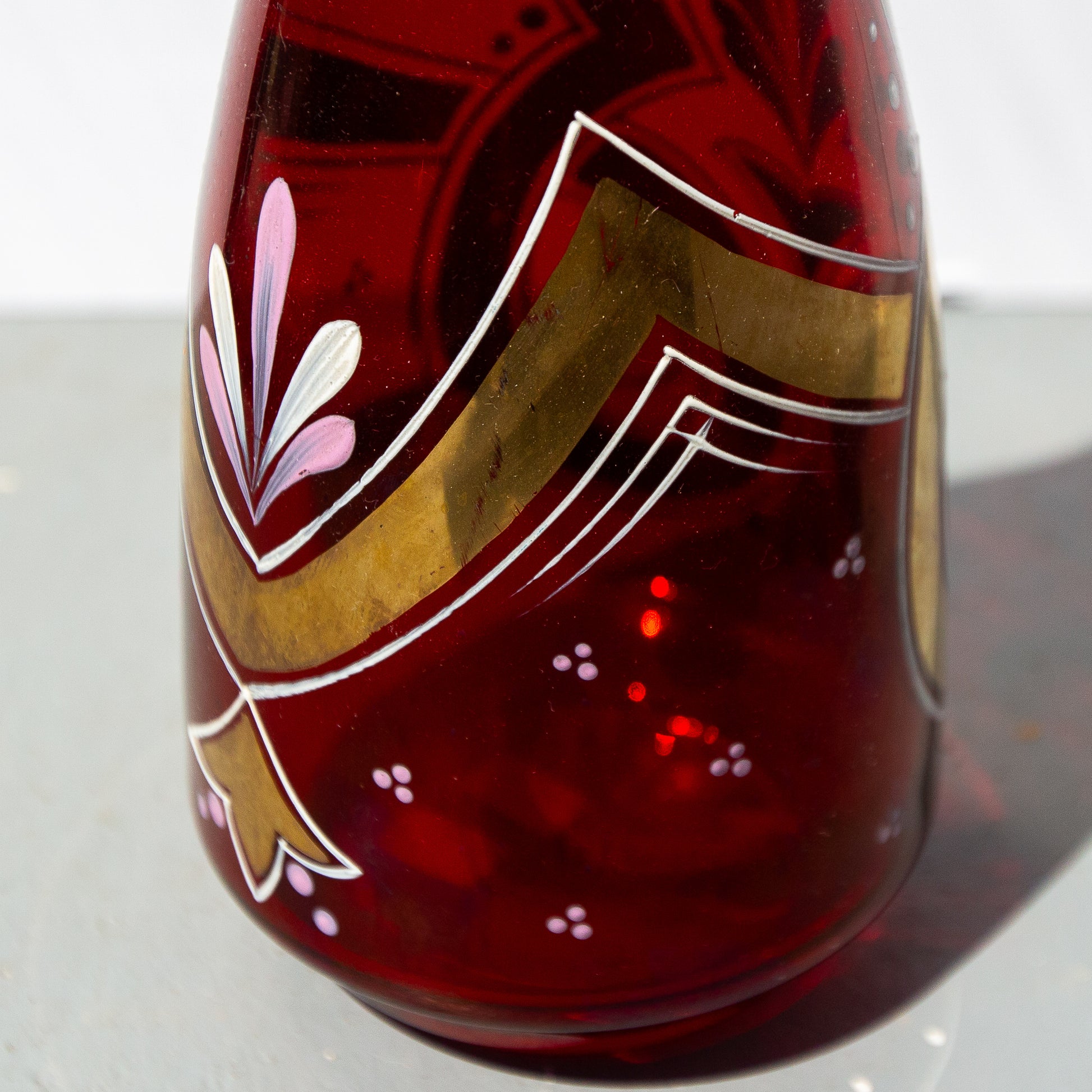 Decorative glass vase with red base and gold and white floral design on a white background