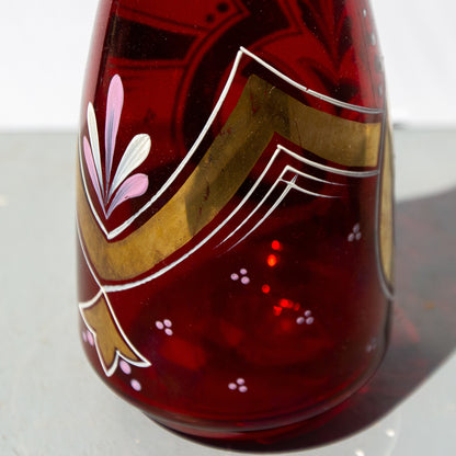Decorative glass vase with red base and gold and white floral design on a white background