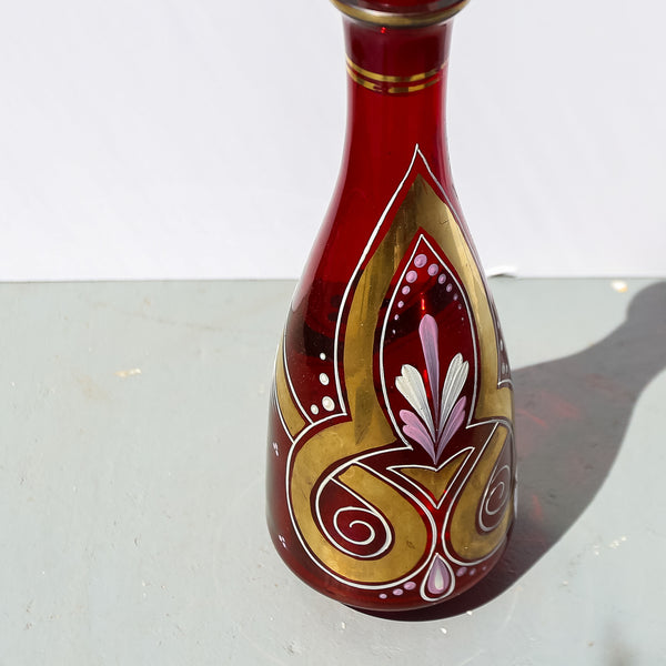 Decorative red glass bottle with gold and pink designs on a white background