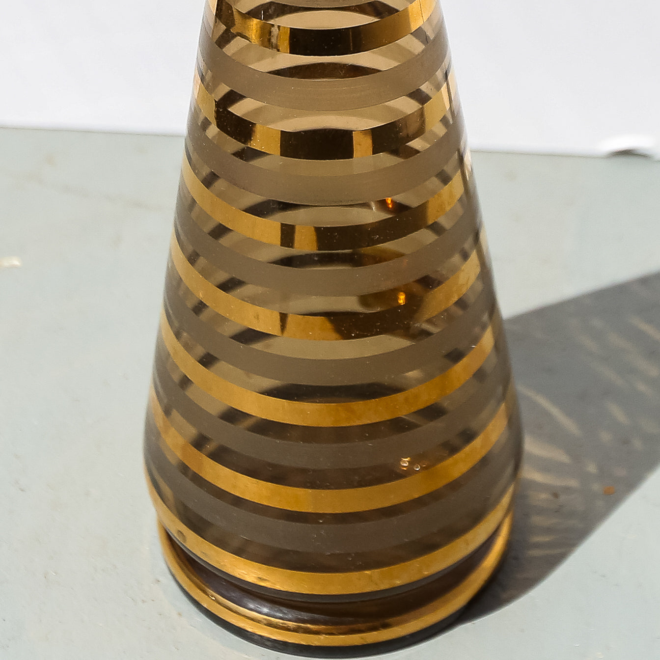Tall, cylindrical vase with concentric gold stripes on a reflective surface
