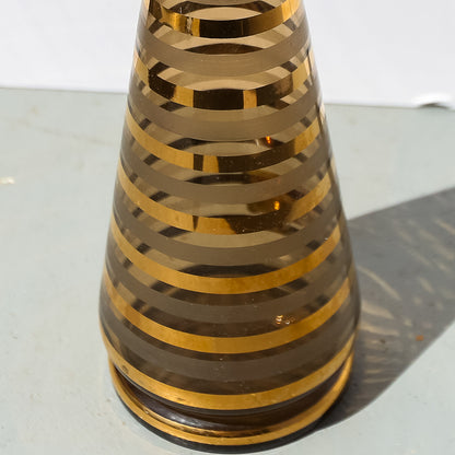 Tall, cylindrical vase with concentric gold stripes on a reflective surface