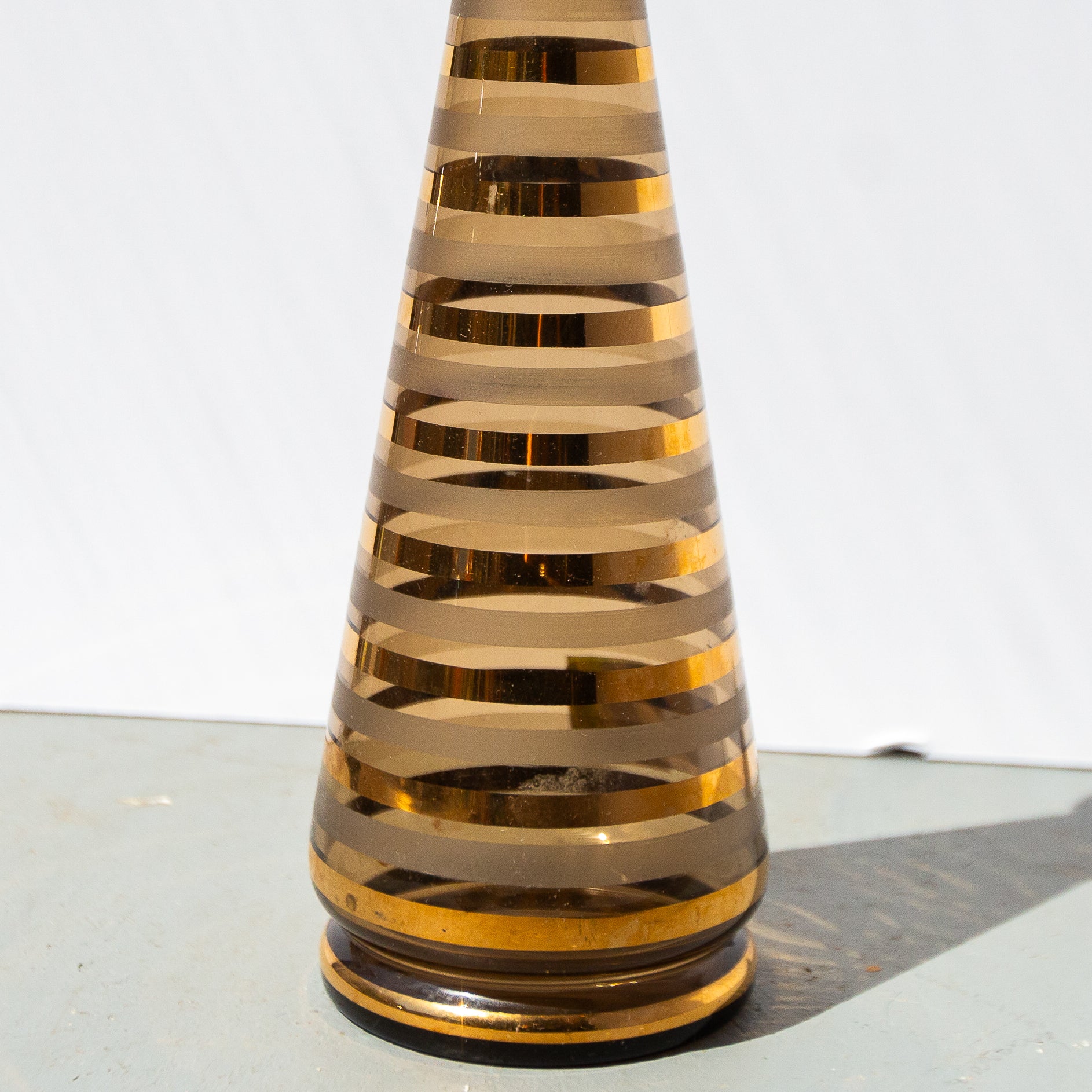 Tall, cylindrical decorative object with gold and bronze stripes on a white background