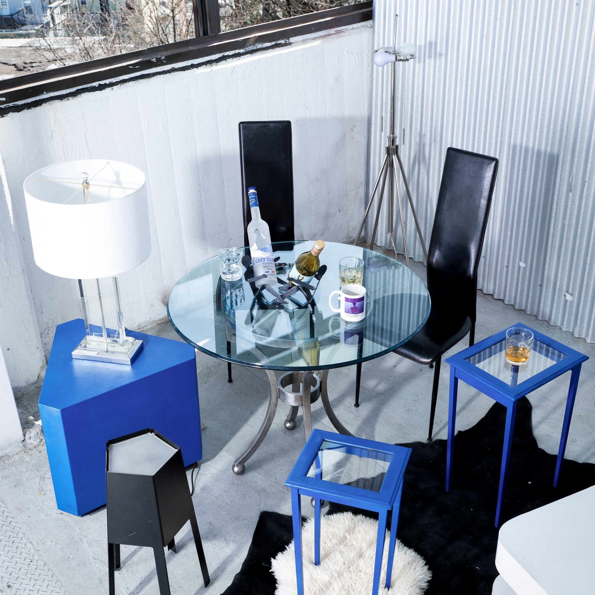 Modern dining area with glass table, black chairs, and blue side tables.