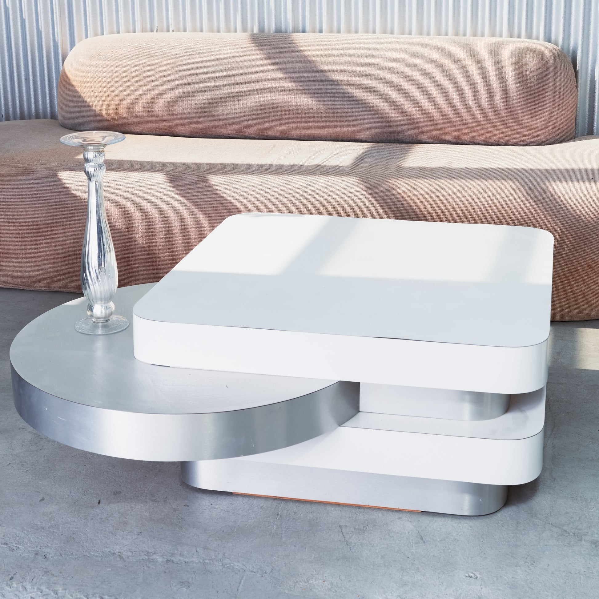 Modern white coffee table with a glass vase on a concrete floor.